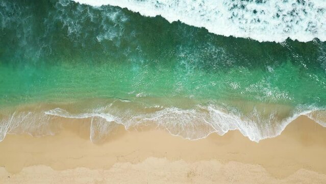 Aerial view of an empty sandy beach with slow moving beautiful waves on a sunny day.