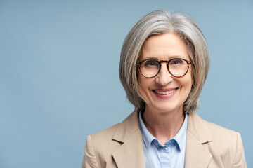 Smiling confident business woman, lawyer, financier wearing stylish glasses looking at camera isolated on blue background. Portrait of confident gray haired politician. Successful business, career  - obrazy, fototapety, plakaty