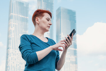 Middle aged woman with red hair stands in a modern business district and and looks at the...