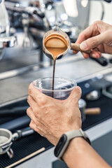 Barista pouring coffee from to plastic cup in coffee shop