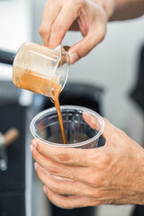 Barista pouring coffee from to plastic cup in coffee shop