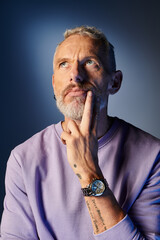 good looking bearded mature man with accessories in casual attire looking away on blue backdrop