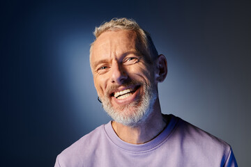 cheerful attractive mature man with gray beard and casual trendy attire smiling happily at camera