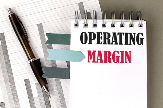 OPERATING MARGIN text on notebook with pen, calculator and chart on a grey background