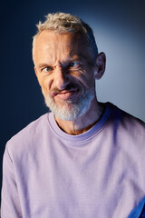 Obraz premium good looking mature man with beard and casual fashionable attire grimacing actively on blue backdrop