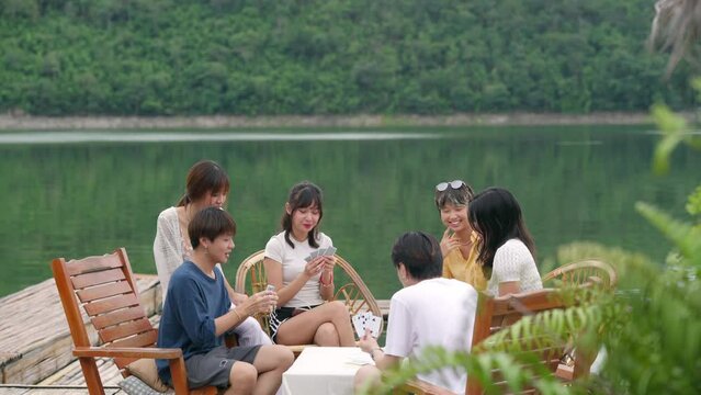 Group of Young Asian man and woman enjoy and fun outdoor lifestyle travel nature forest mountain on summer holiday vacation. Generation z people friends playing cards together on lake house balcony.