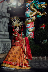 Fototapeta premium portrait of a woman. person in traditional costume. woman in traditional costume. Beautiful young woman in a bright red dress and a crown of Chinese Queen posing against the ancient door. 