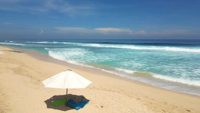 Lone umbrella with stuff on a sandy wild beach against the slow waves of the Indian Ocean during high tide on a sunny day.