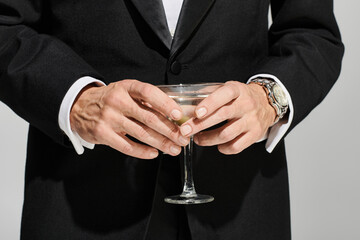 cropped view of glass of delicious martini with green olives in it in hands of mature elegant man