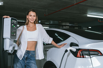 Young woman travel with EV electric car to shopping center parking lot charging in downtown city...