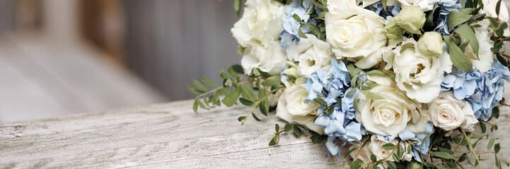 An elegant bouquet with blooming white roses and delicate blue flowers rests on a wooden railing....