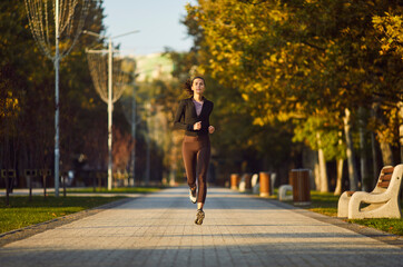 Fototapeta premium Female young runner jogging alone in city park. Healthy sporty fitness woman running outdoors training for wellness, health and cardio. Workout in nature and healthy lifestyle concept.