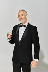 handsome bearded mature male model  in elegant tuxedo holding martini glass and looking at camera