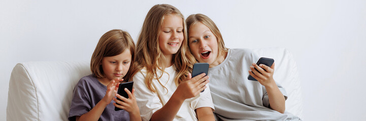 Three girls use smartphones on the sofa. Three sisters smiling in casual clothes against a white...