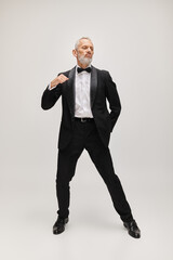 Fototapeta na wymiar attractive bearded mature man in debonair black tuxedo with bow tie posing in motion while dancing