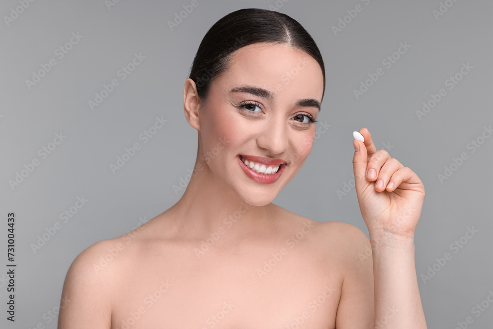 Wall mural beautiful young woman with vitamin pill on grey background