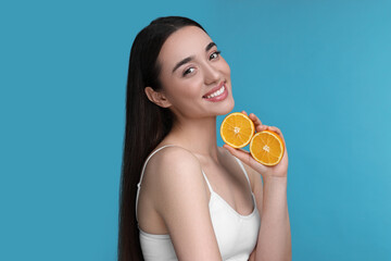 Beautiful young woman with pieces of orange on light blue background