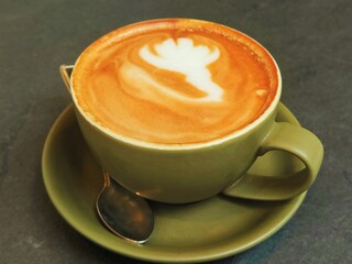 Green cup of coffee and little spoon on the black table 