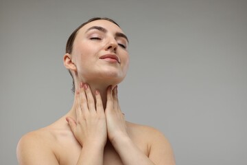 Beautiful woman touching her neck on grey background. Space for text