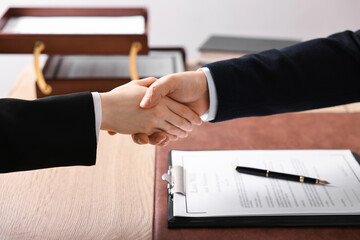 Notary shaking hands with client at wooden table in office, closeup