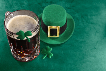 St. Patrick's day. Beer, decorative clover leaves and leprechaun hat on green table, space for text