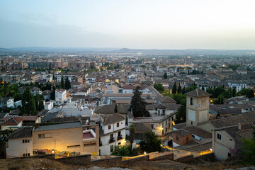 Cityscape view of Granada city centre at late evening, blue hour, overlooking white buildings with traditional tile terracotta, street lights and trees. Copy space background no people or logos