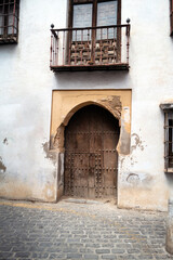 Fototapeta na wymiar A rustic door in a latin architecture style, that could be from Europe or America, surrounded by a road, wall and foliage. Backdrop for graphic resource or decorative copy space.
