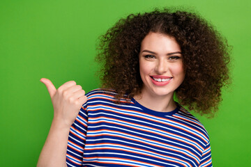 Photo of nice positive girl beaming smile indicate thumb finger empty space isolated on green color...