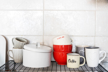 Gray and white cups with hearts and the inscription - I love you on a shelf in the kitchen against the background of a gray tiled wall.