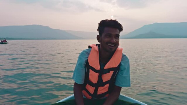 Smiling fisher man wearing a life jacket sitting on a speed boat talking with guest a serene sea or lake and hills in the background at dusk
