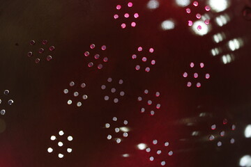 Metal perforado en forma de círculos o rosetas de un colador de pasta, con luz roja y blanca atravesando los agujeros formando un original diseño abstracto con fondo negro