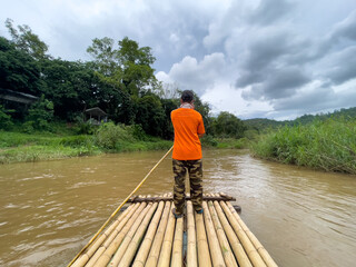 Man rowing bamboo raft. Man uses a bamboo to push a raft on a river and see the nature of the forest on both sides.
