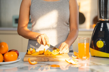 Close up shot of woman slicing oranges of making juice at morning in kitchen - concept of healthy...