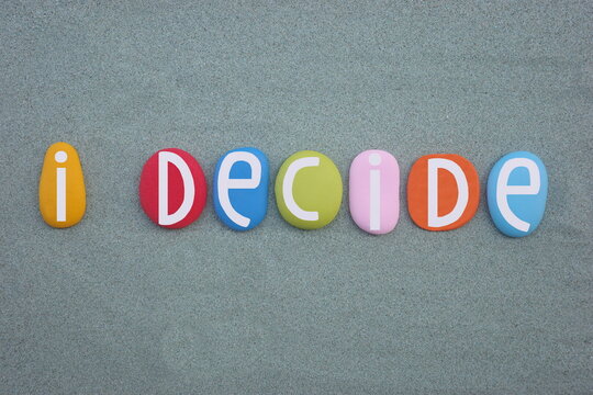 I decide, motivational text composed with hand painted multi colored stone letters over green sand