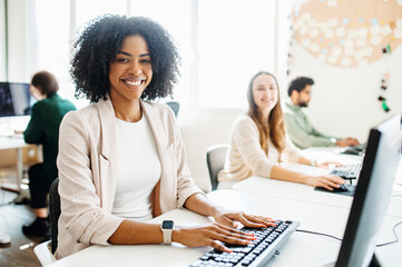A cheerful female employee with curly hair radiates positivity, as she engages with her work on a...