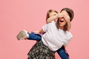 Laughing little girl covering mother's eyes while smiling woman giving her daughter piggyback ride...