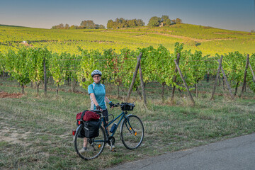 Mittelbergheim, France - 09 10 2020: Alsatian Vineyard. A woman dressed in a blue t-shirt, black shorts and a helmet, poses next to her blue bicycle with vine fields behind.