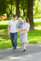 Obraz premium Happy young family goes to the park for a walk, the mother carries the child in her arms.Happy family moments,parenthood