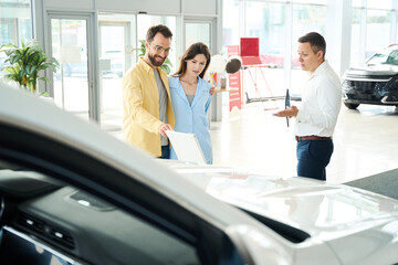 Fototapeta premium Couple in a car dealership communicates with a consultant
