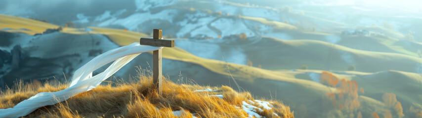 Windswept white scarf wrapped around simple wooden cross standing atop a grassy cliff overlooking a...