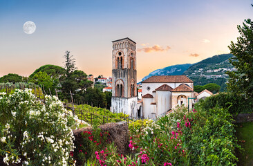 Ravello, Italy. Breathtaking sunset over the Cathedral of Santa Maria Assunta and its bell tower framed between plants and colorful oleander flowers. Big Moon on the left.