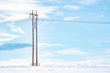Isolated power pole on a snow covered prairie field with overhead power lines and cables on the Canadian prairies in Rocky View County Alberta.