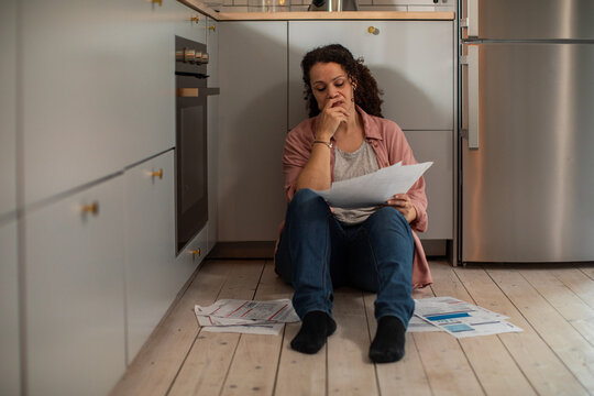 Worried woman on kitchen floor reading bills