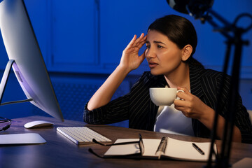 Tired overworked businesswoman drinking coffee at night in office