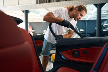 Long-haired man is vacuuming the inside of a car