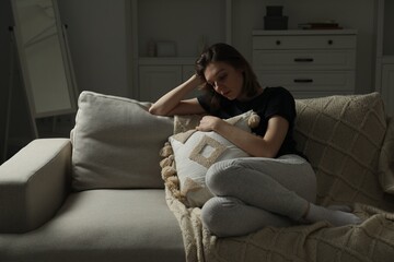 Obraz premium Sad young woman sitting on sofa at home