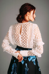 Embroidery long sleeve blouse in white, rear view. Studio portrait of young beautiful ginger lady. Natural makeup and hairdo with red lips. Evening outfit,  female fashion. Transparent elegant dress.
