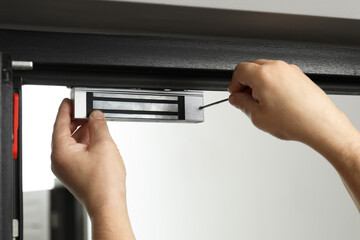 Man with screwdriver installing electromagnetic door lock indoors, closeup. Home security