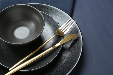 Stylish ceramic plates, bowl and cutlery on dark blue background, closeup