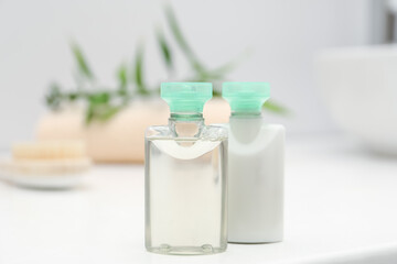 Mini bottles of cosmetic products on white table against blurred background